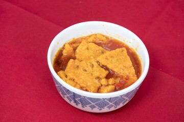 Top view of Gujarati Kathiyawadi Spicy Dhokali Sabji, on bowl dish prominently, set against a red background