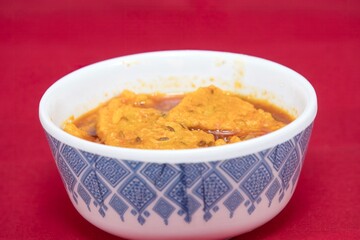 Side view of Gujarati Kathiyawadi Spicy Dhokali Sabji, on bowl dish prominently, set against a red background