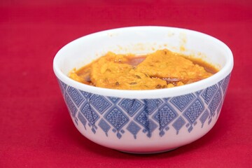 Side view of Gujarati Kathiyawadi Spicy Dhokali Sabji in bowl dish prominently, set against a red background