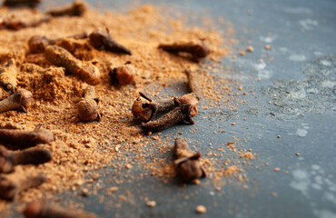 Fresh whole and ground clove spice on a dark blue backdrop, evoking winter warmth.