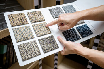 Designer hand pointing at sample fabric pieces on carpet swatch collection. Customer choosing color...