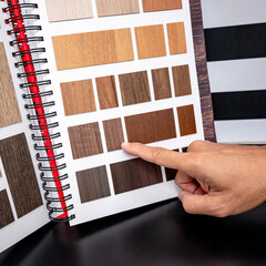 Designer hand pointing at wooden laminate swatch collection in material sample catalog. Customer choosing natural wood texture for furniture finishing or interior architecture design.