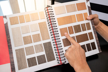 Designer hand pointing at wooden laminate swatch collection in material sample catalog. Customer...