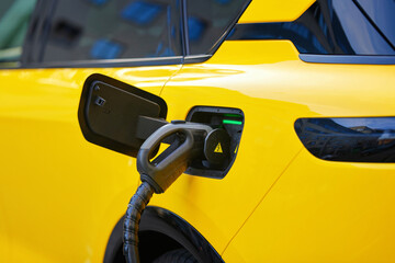 Electric car charging at power station, closeup view on connected plug to vehicle's charging port...