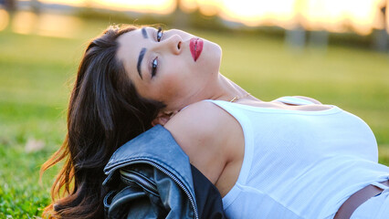 A beautiful young brunette woman posing for the camera on a sunny day in a tree-filled park