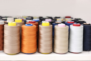 Many different spools of thread on white shelf in professional workshop