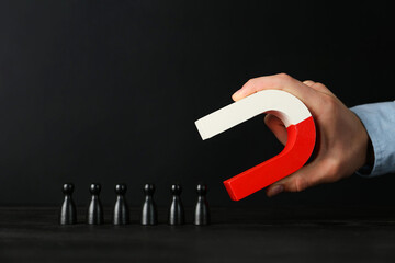 Man with magnet attracting black pieces at wooden table, closeup
