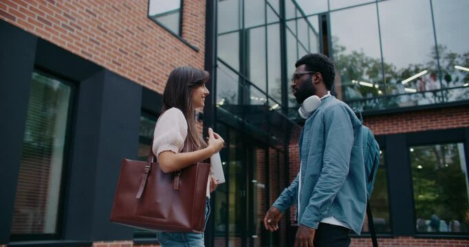 African American male standing in front of girl while answering question or explaining. Woman listening with focus. Man helping newcomer in business team with information. Supporting others.