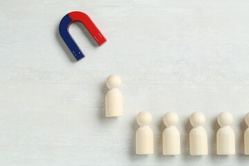 Magnet attracting human figure among other ones on white table, flat lay