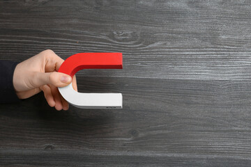 Woman with horseshoe magnet on wooden background, top view. Space for text