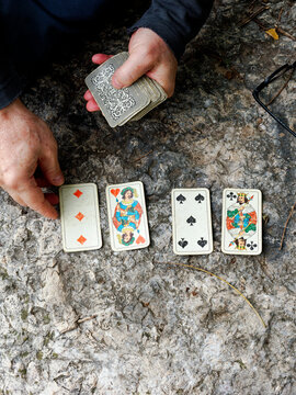 Hands laying out playing cards on a rocky surface outdoors, Italy