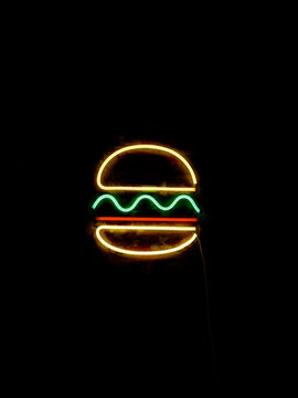 Neon sign of a hamburger glowing in the dark.