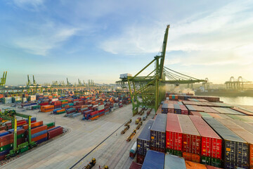 Sunrise over a busy container port with rows of colorful shipping containers, large cranes, and cargo handling equipment, Singapore
