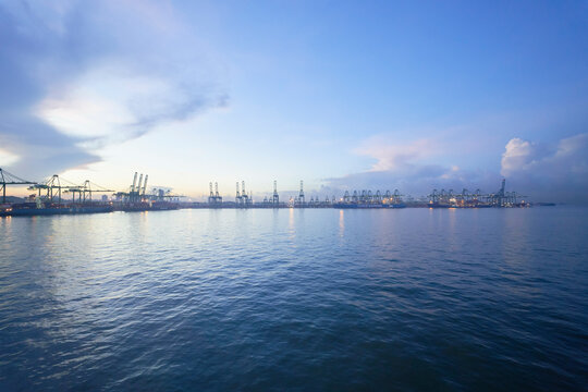 Serene seascape at dusk with illuminated port cranes on the horizon under a vast sky, Singapore