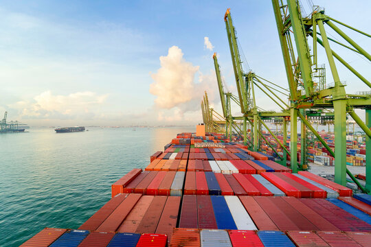 Cargo ship loaded with colorful containers at dock with cranes under a clear sky at sunrise, Singapore
