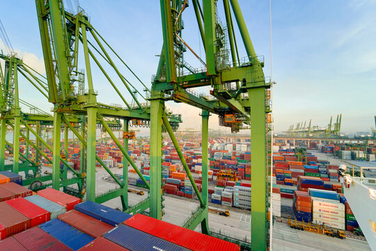 Aerial view of a bustling container port with rows of colorful shipping containers and large cranes against a clear sky, Singapore