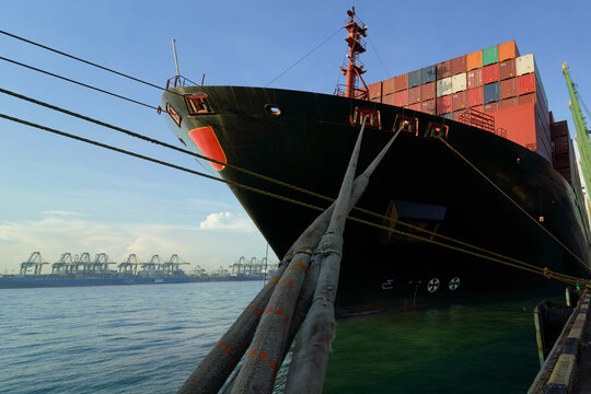 Cargo ship loaded with containers moored at a commercial dock with cranes in the background under a blue sky, Busan, Korea
