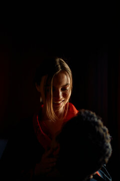 Woman in a red sweater embracing her partner in a dimly lit room.