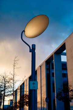 Streetlight glowing at dusk next to a bicycle lane sign with a building and a tree silhouetted against a colorful sky, Berlin, Germany