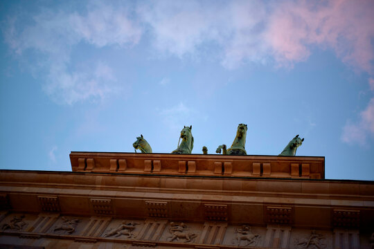 Sunset behind the Brandenburger Gate with a row of sculpted horses on the rooftop against a cloudy sky, Berlin, Germany