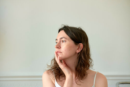 Woman deep in thought with her hand on her cheek against a neutral background