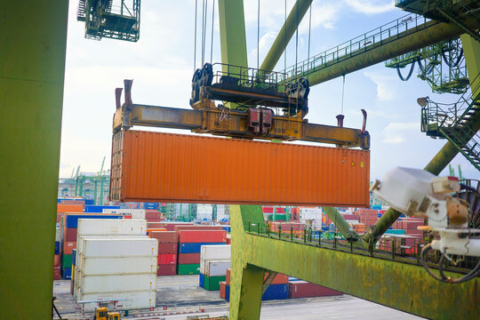 Container being moved by a crane at a cargo port with various shipping containers stacked in the background, Singapore