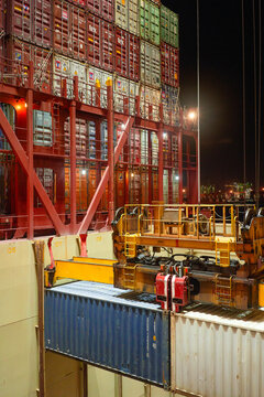 Night view of a bustling container terminal with stacked shipping containers and industrial machinery under artificial lighting, Singapore