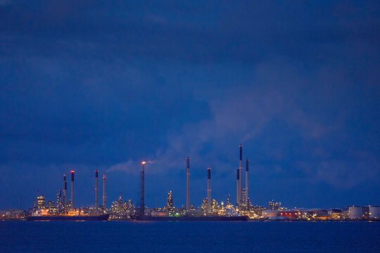 Industrial skyline at dusk with illuminated refinery towers against a deep blue sky, Singapore
