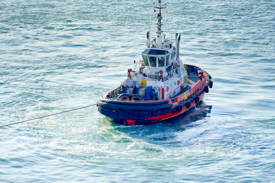 Red and blue tugboat towing a large unseen vessel on the open sea, Singapore