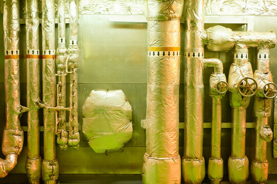 Industrial pipes and valves insulated with reflective foil in a mechanical room on a cargo ship