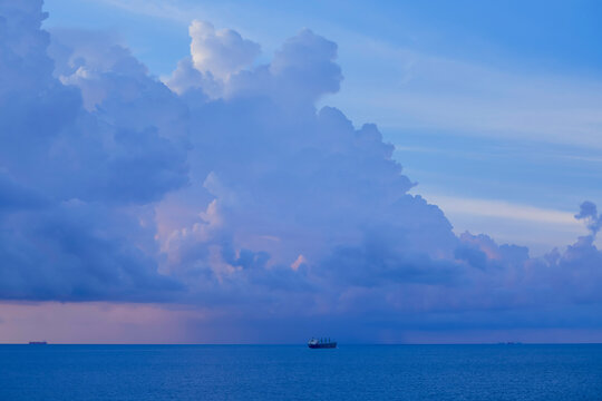 Serene ocean view at dusk with large cumulus clouds and a distant cargo ship, South China Sea
