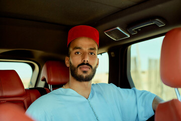 Confident young man in a blue shirt and red cap sitting in a car with a stylish red leather interior, Morocco