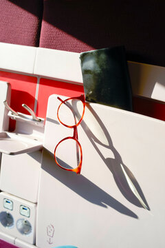 Red glasses casting a shadow on an open white tray against a red and white backdrop in a train seat row