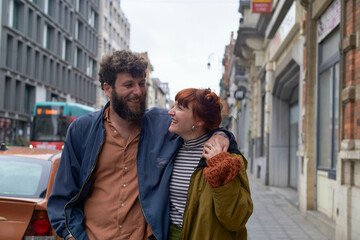Smiling couple embracing on a city street with buildings and a bus in the background, Brussels, Belgium