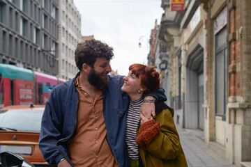 Joyful couple embracing and smiling at each other on a bustling city street with vehicles and buildings in the background, Brussels, Belgium