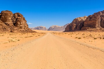 Endless Desert Road with Majestic Rocky Cliffs Under Clear Blue Sky