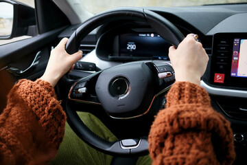 Close-up of a person's hands on a steering wheel with a modern car dashboard in the background.