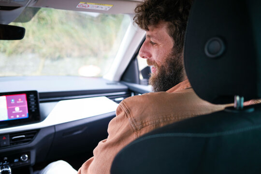 Man with a beard is passenger in a car, looking at the road ahead, with the interior and dashboard clearly visible.