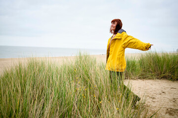 Woman in a yellow raincoat enjoying the calm at a beach with tall grass, Belgium