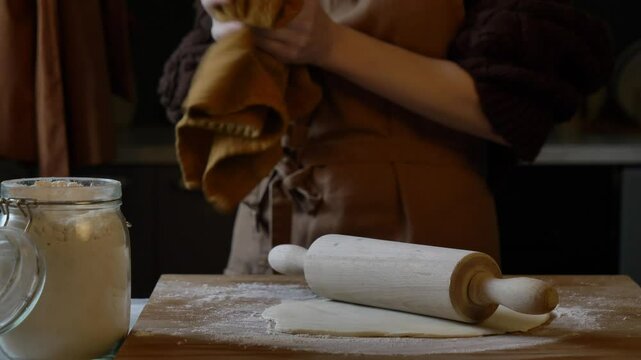 woman in an apron rolling out dough with a rolling pin to make dumplings in her kitchen