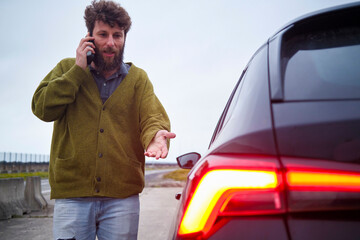 Man on a phone call standing next to a car with its taillights on, , Belgium