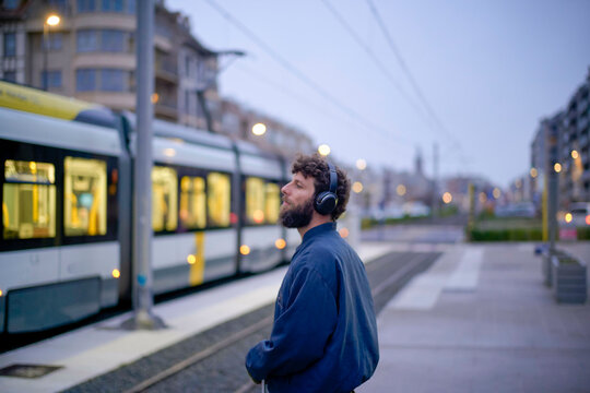 Man with headphones standing by a tram at twilight, Belgium