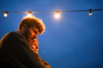 Couple embraces under a string of lights against a twilight sky, Belgium