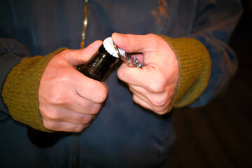 Close-up of a person in a green sweater opening a brown beer bottle with a white lid.