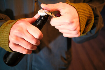Close-up of hands using a bottle opener to uncap a beer bottle.