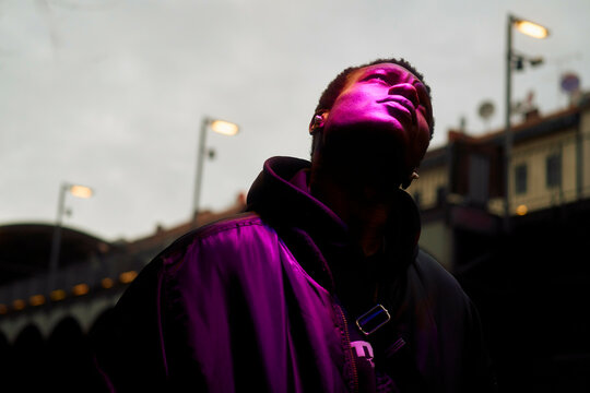 Silhouette of a young black man gazing upward with a purple light illuminating their face against an evening sky, Berlin, Germany