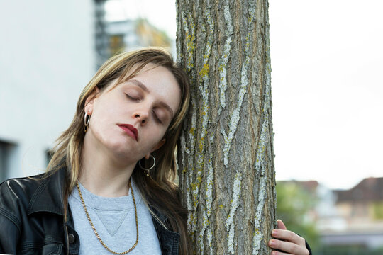 Woman resting her head against a tree trunk with her eyes closed in a moment of relaxation.