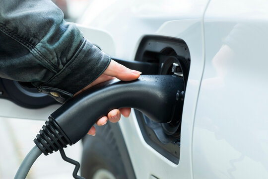 Close-up of a hand plugging in an electric vehicle charging cable to a white car.