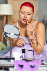 Fototapeta premium A young woman applies lipstick at home, surrounded by beauty products.
