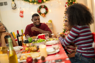 A warm Christmas family dinner with a father serving food to his young child, surrounded by festive decorations, a Christmas tree, and a holiday table spread. Joyful and cozy holiday atmosphere.